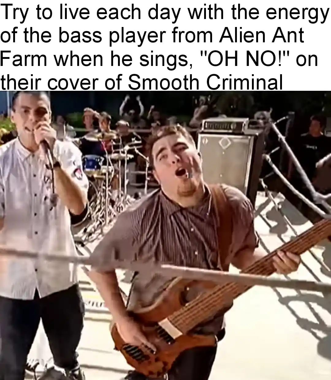 A still from a music video shows a bass player with an exaggerated, intense facial expression while playing his instrument…