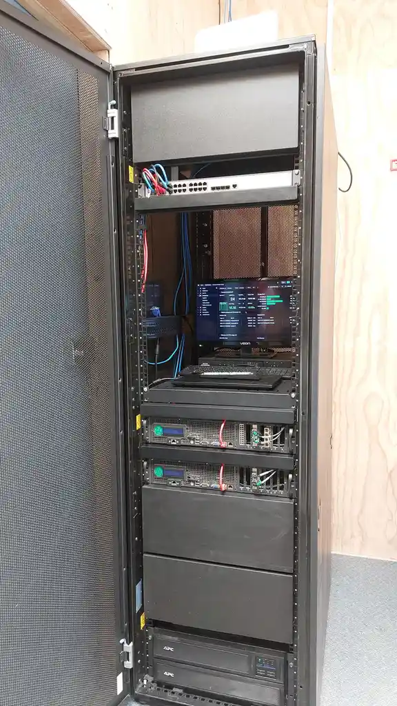 A server rack with its door open, revealing multiple server units, a monitor displaying system stats, and various cables…