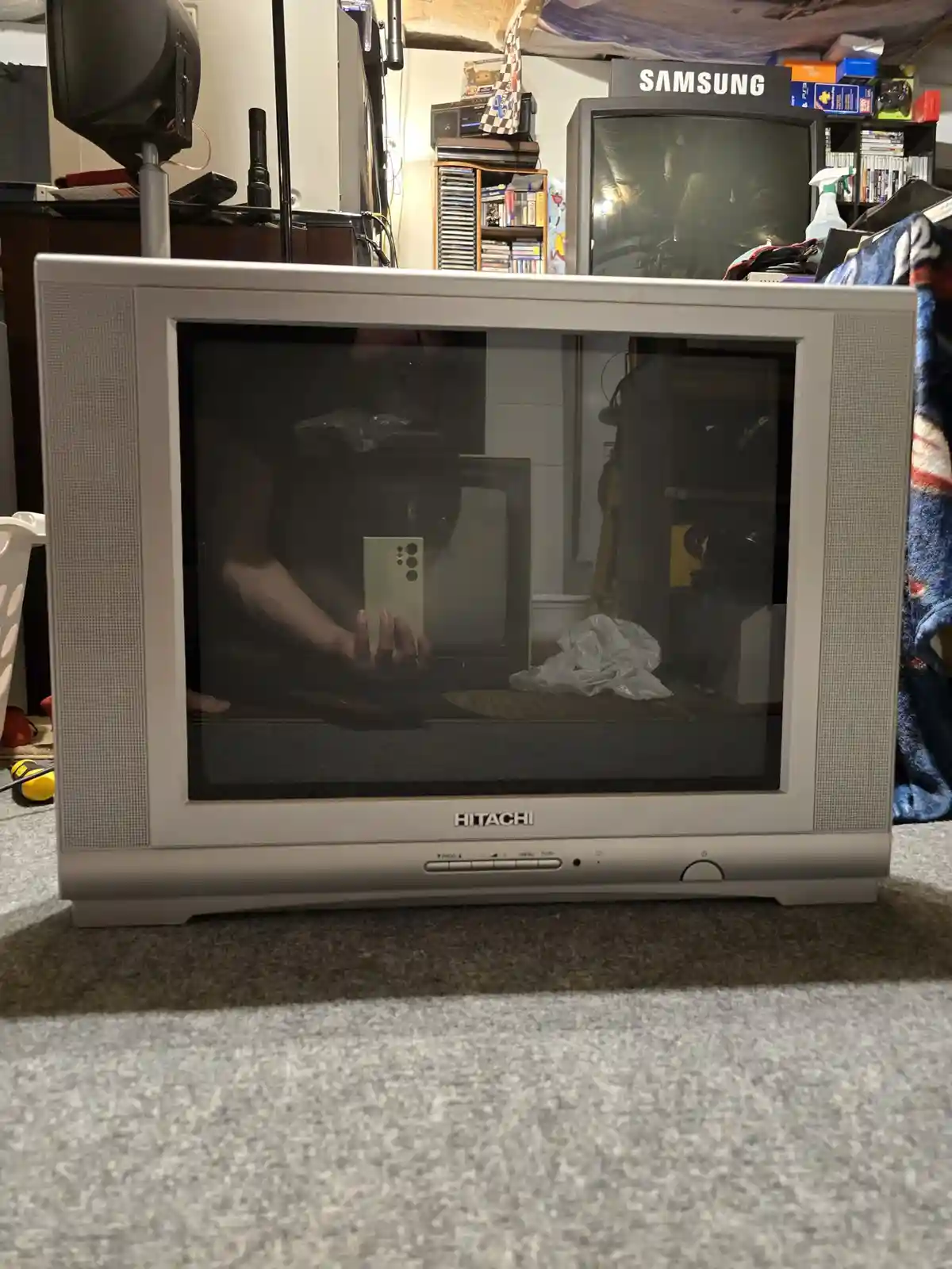 A person is taking a photo of an old Hitachi CRT television with their smartphone, and the reflection in the TV's screen…