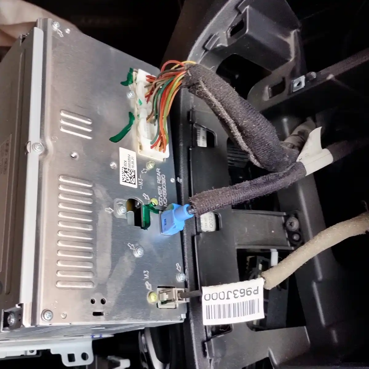 A close-up photo shows the back of a car's radio unit with exposed wiring, connectors, and screws. The unit is partially…