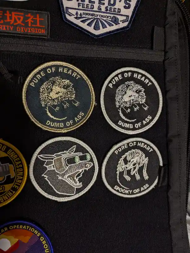A close-up of a black backpack covered in embroidered patches, including four circular ones featuring animal illustrations…