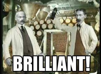 Two men in white lab coats stand in a brewery or distillery with copper stills and wooden barrels in the background. The man…