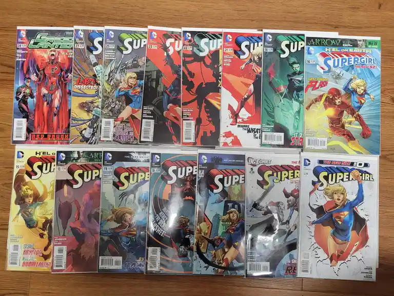 A collection of DC Comics featuring Supergirl and related characters, arranged in two rows on a wooden surface. The covers…