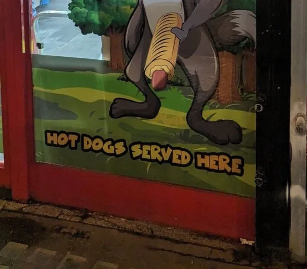 A cartoon illustration of a grey wolf holding a hot dog in its paws is painted on a red door. Below the wolf, bold yellow…