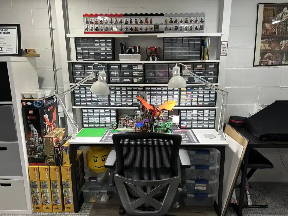 A meticulously organized LEGO enthusiast's workspace features a large white desk with a black ergonomic chair, flanked by…