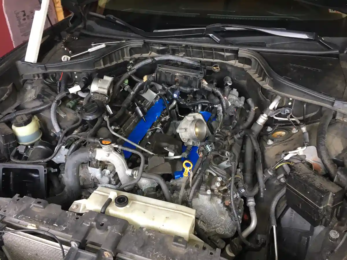 A close-up photo of a car's engine bay with the hood open, showing a newly installed engine with a bright blue intake…