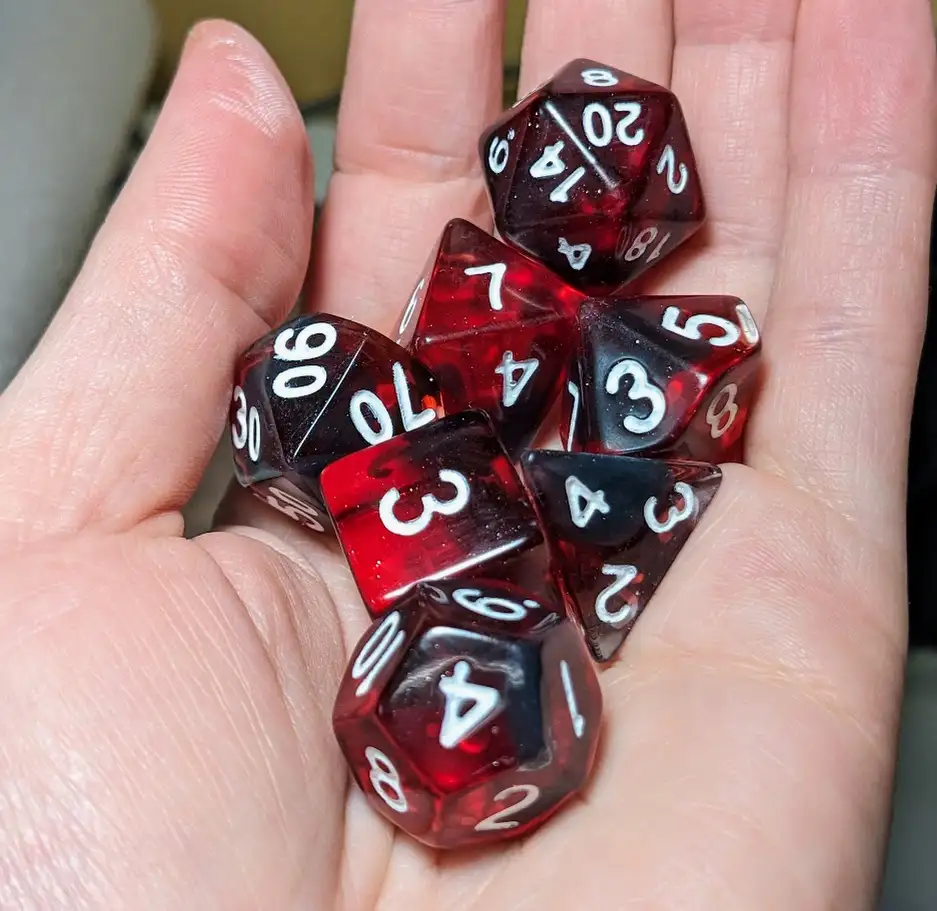 A hand holds a pile of translucent red and black polyhedral dice showing various numbers, including a 20 on the top die. The…
