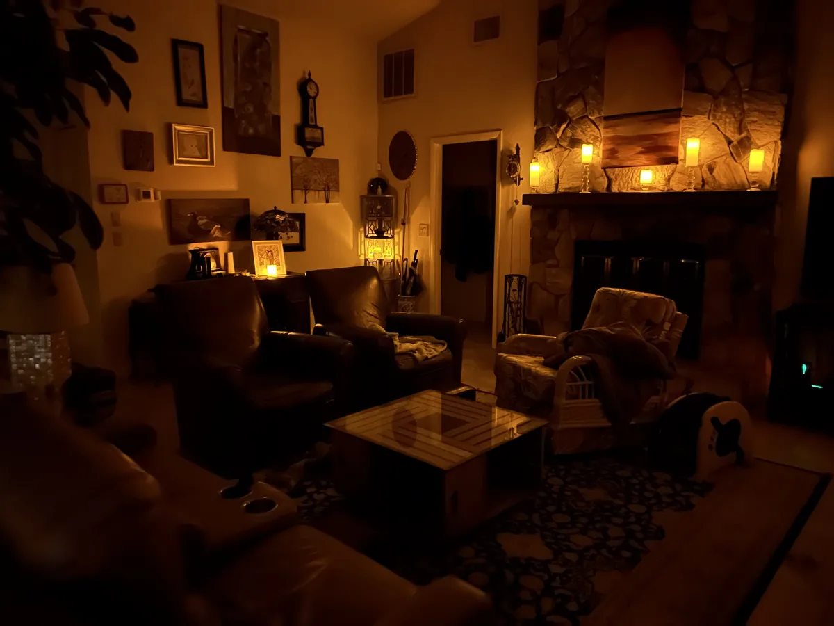 A dimly lit, cozy living room with warm candlelight, leather chairs, a stone fireplace, and a patterned rug. The overlaid…