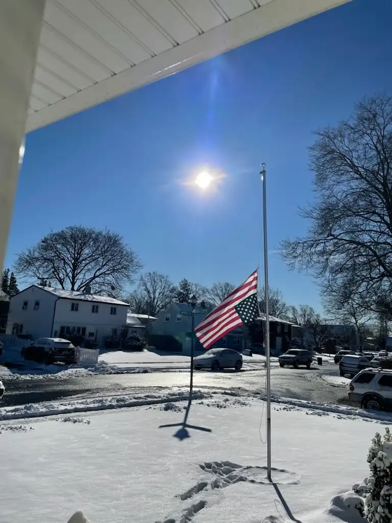 A bright, sunny winter day with a clear blue sky and the sun shining brightly. An American flag is flying at half-mast on a…