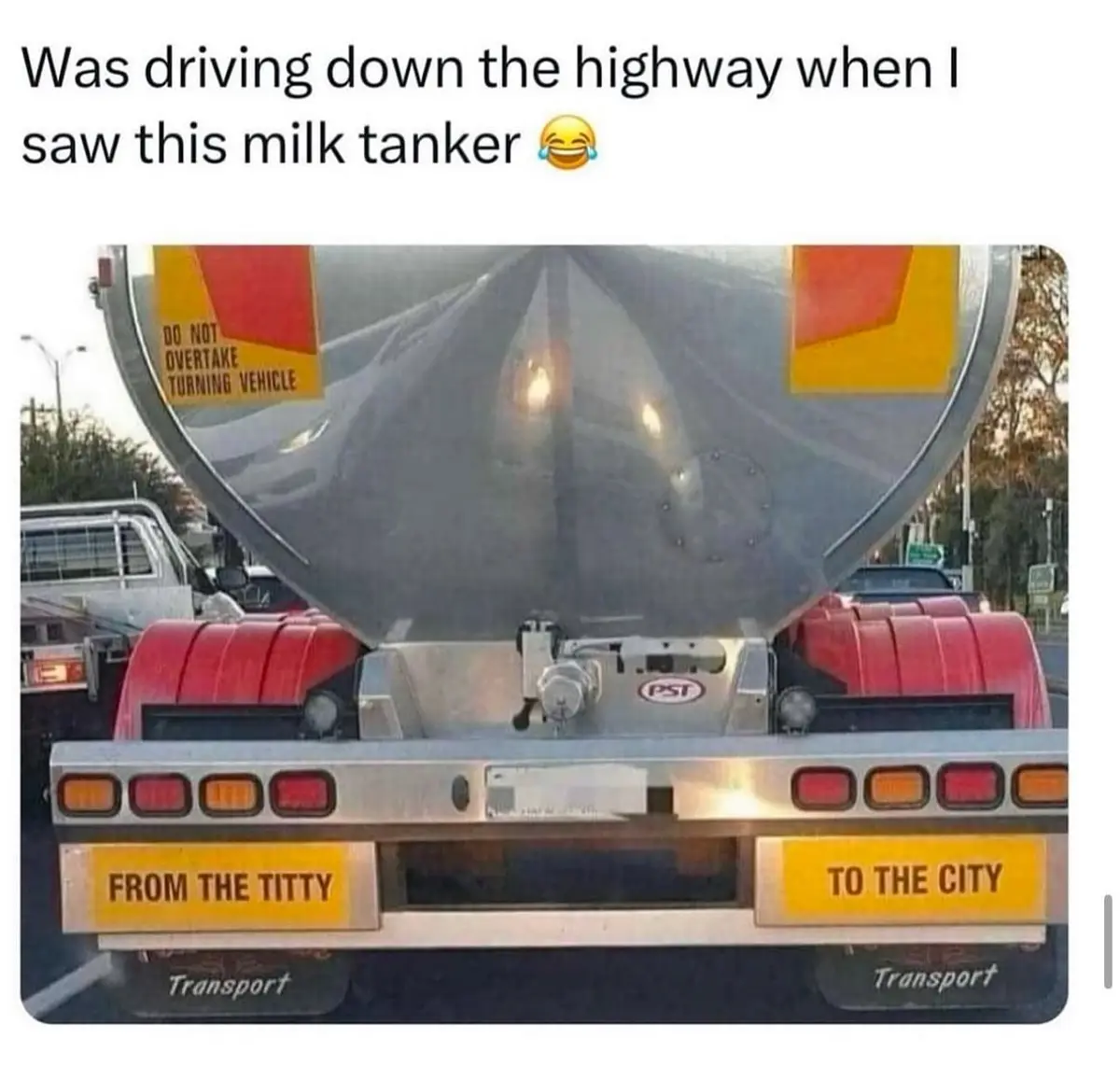 The image shows the rear of a large silver milk tanker truck with red fenders and taillights. Two yellow signs on the bumper…