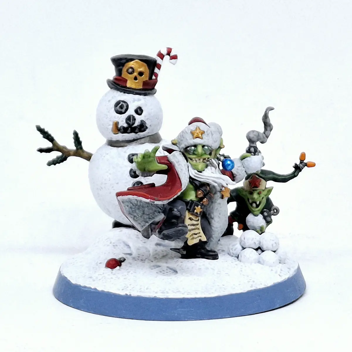 A painted miniature figurine shows a snowman with a skull top hat and candy cane, alongside two green goblin-like figures…