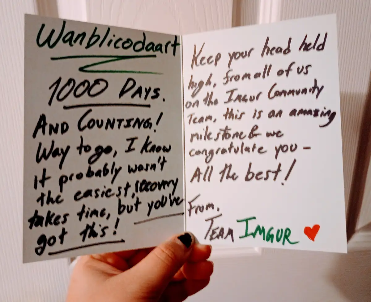 A hand holds an open handwritten card celebrating 'Wanblicodaart' reaching 1000 days, with encouraging messages from the…