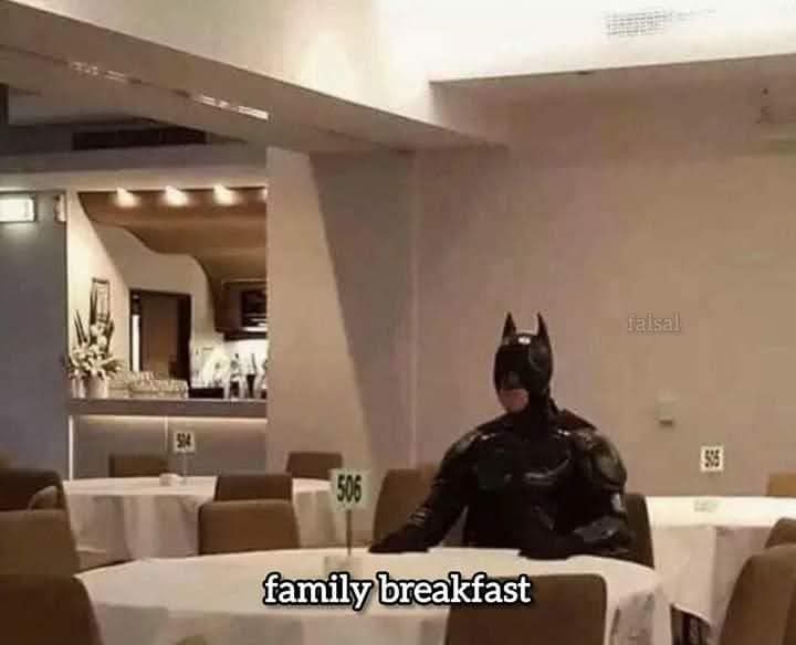A person in a full Batman costume sits alone at a table in a restaurant, with table numbers 504, 505, and 506 visible…
