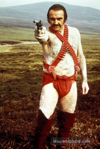 A man with a mustache, wearing a white textured outfit with red suspenders and red underwear, holds a pistol pointed forward…