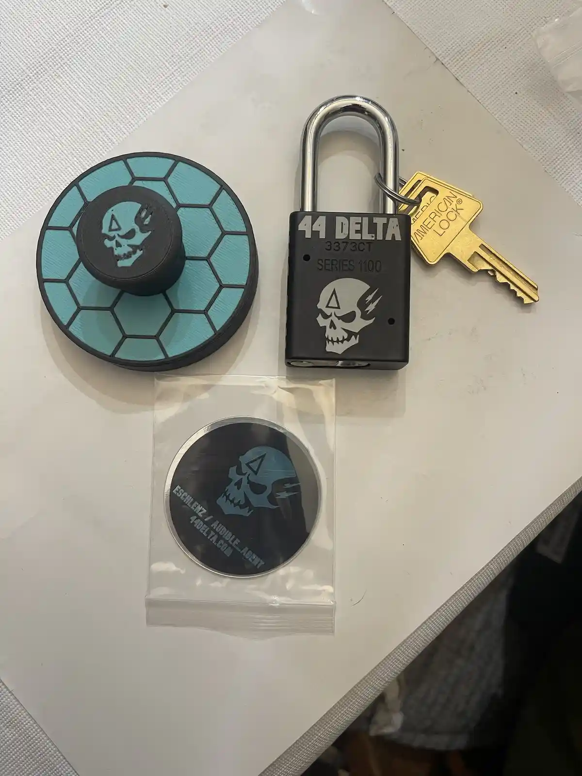 A collection of 44 Delta branded merchandise including a black padlock with a skull logo and key, a teal and black hexagonal…