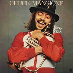 A vintage album cover featuring jazz trumpeter Chuck Mangione, smiling broadly while holding a trumpet, wearing a red…