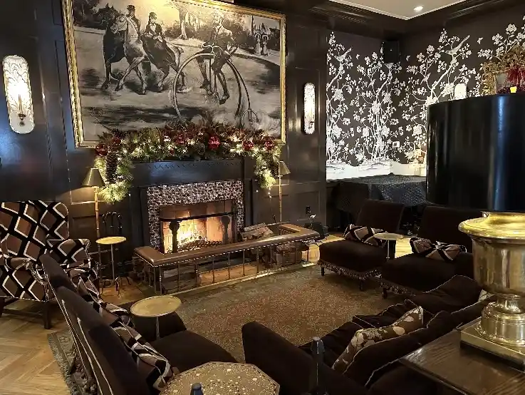 a luxurious, dimly lit hotel lobby features a roaring fireplace adorned with festive garlands, dark wood paneling, and…