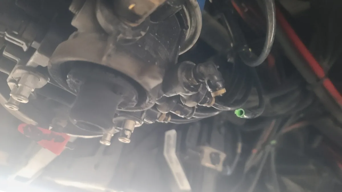 A close-up, slightly blurry photo shows a car's engine bay with various mechanical parts, hoses, and wires. A small green…