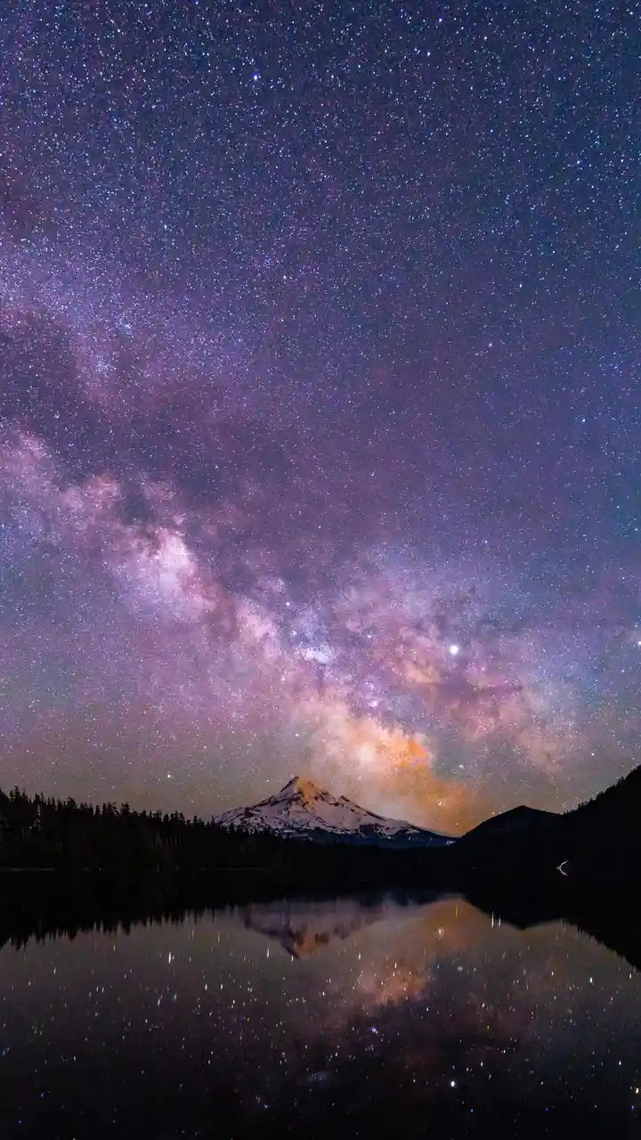 A stunning night sky photograph shows the Milky Way galaxy arching across a purple and blue starfield, reflected perfectly…