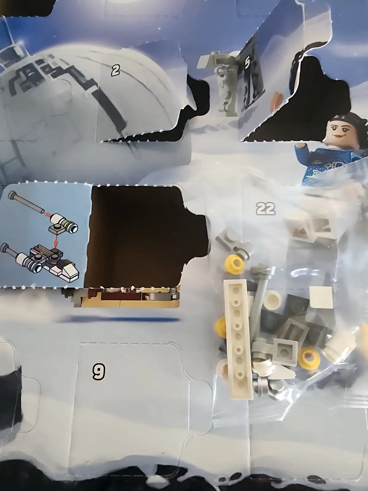 A close-up of a torn LEGO instruction manual showing large, irregularly shaped holes where pieces were removed, revealing…
