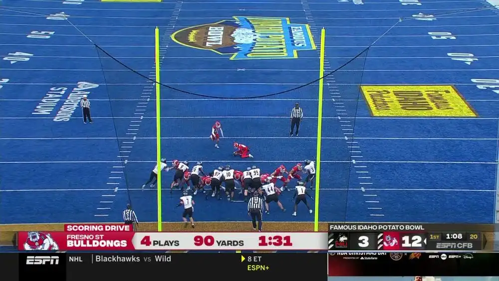 An aerial view of a college football game at the Famous Idaho Potato Bowl, showing the Fresno State Bulldogs huddled near…