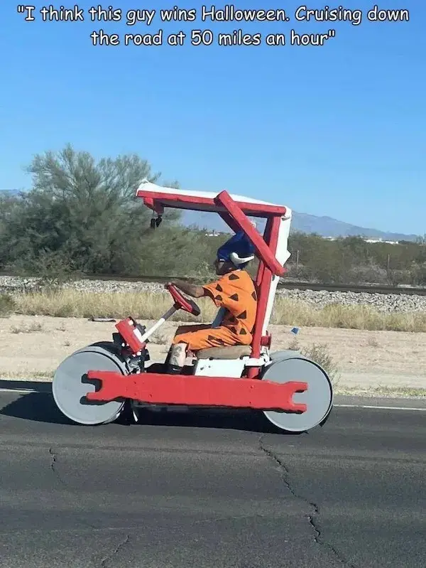 A person dressed in an orange and black spotted caveman costume with a blue helmet is driving a red and white homemade…