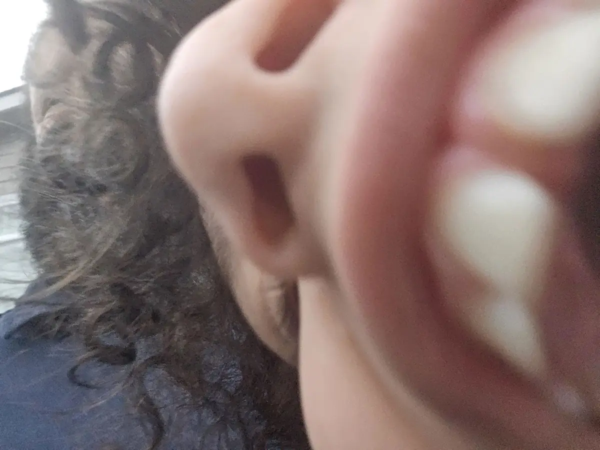 A close-up, blurry selfie showing a person's ear and fingers partially obscuring the view, with dark curly hair visible in…