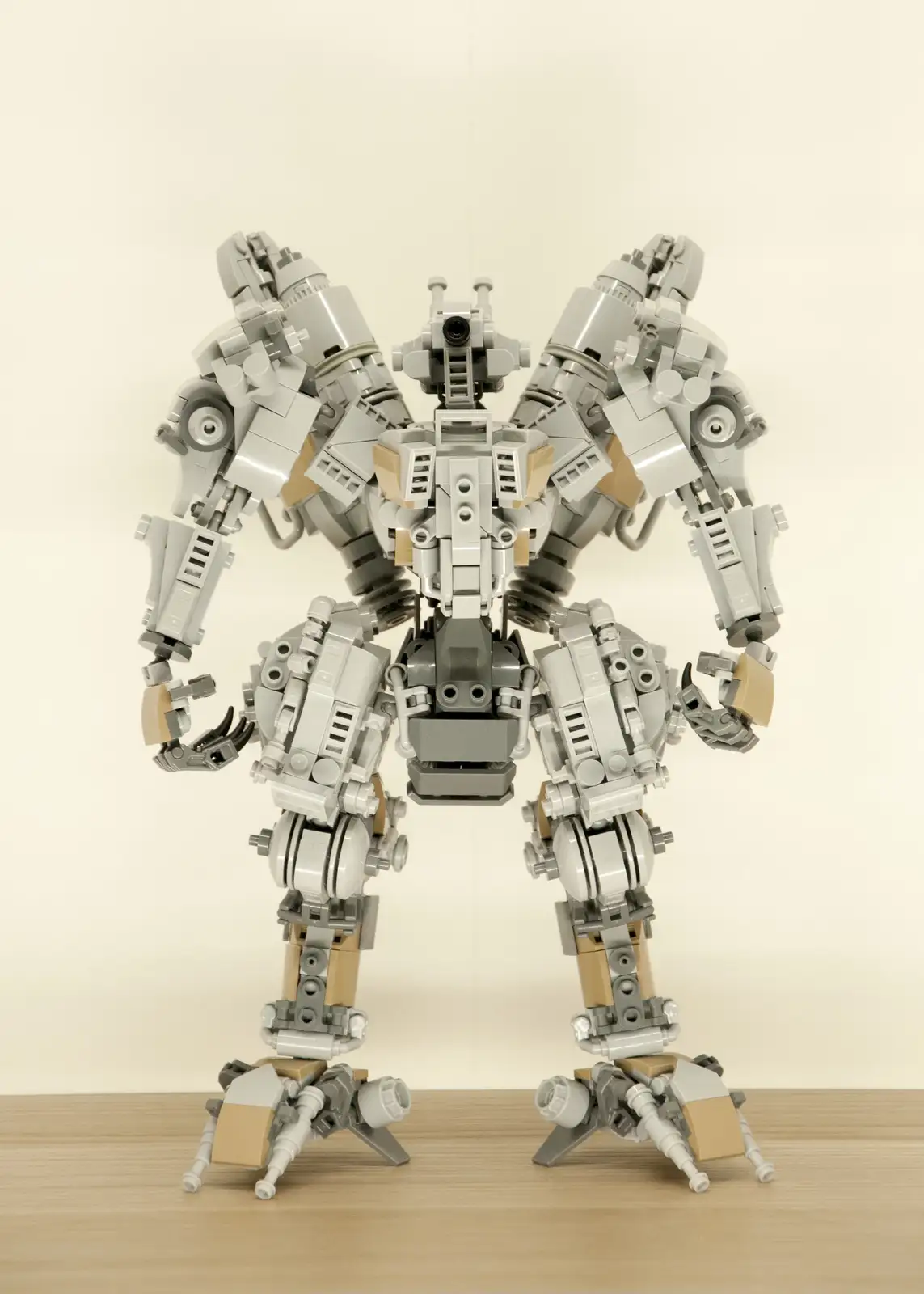 A large, intricate robot built from gray and tan LEGO bricks stands on a wooden surface against a plain background, its arms…