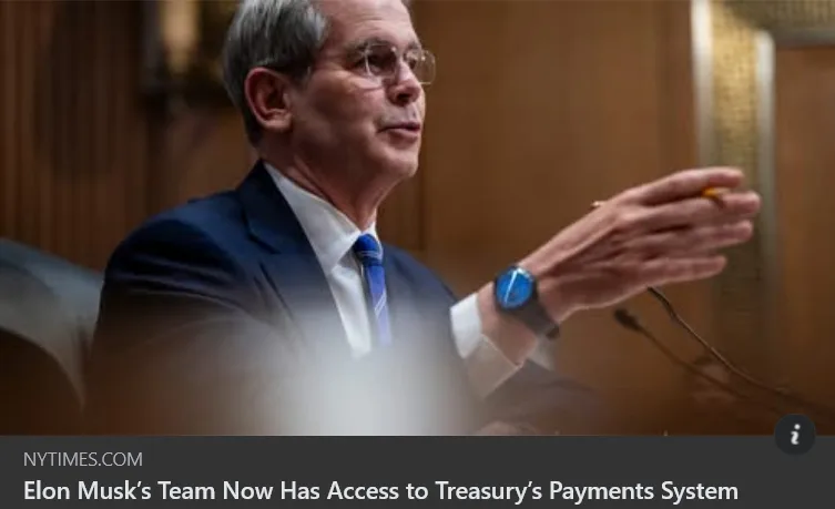 A man in a suit and glasses gestures while speaking, with a blue smartwatch visible on his wrist. The image has a news…