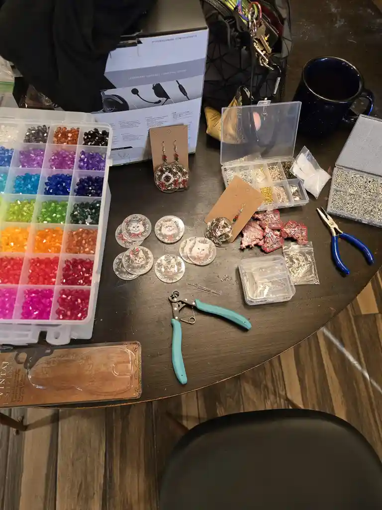 A cluttered crafting table displays a rainbow of organized beads, pliers, and tools, surrounded by finished cat-themed…