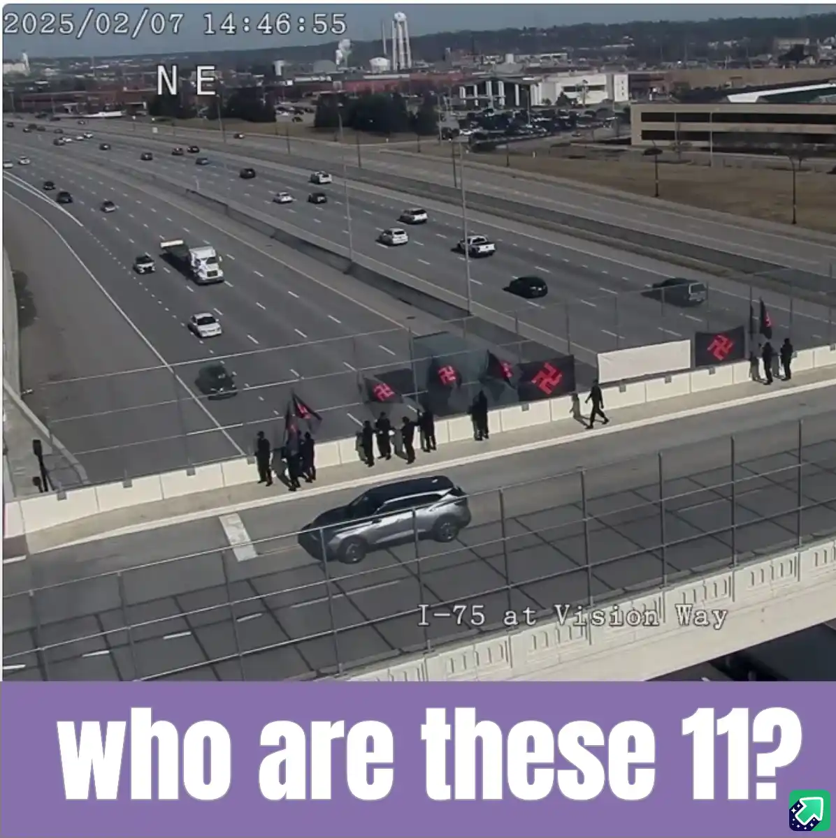 A security camera image from I-75 at Vision Way shows 11 people standing on a highway overpass, holding black flags with red…