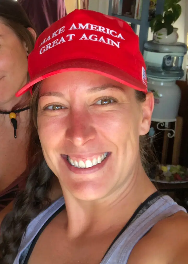A smiling woman wearing a red baseball cap with the white text 'MAKE AMERICA GREAT AGAIN' embroidered on the front, taken…