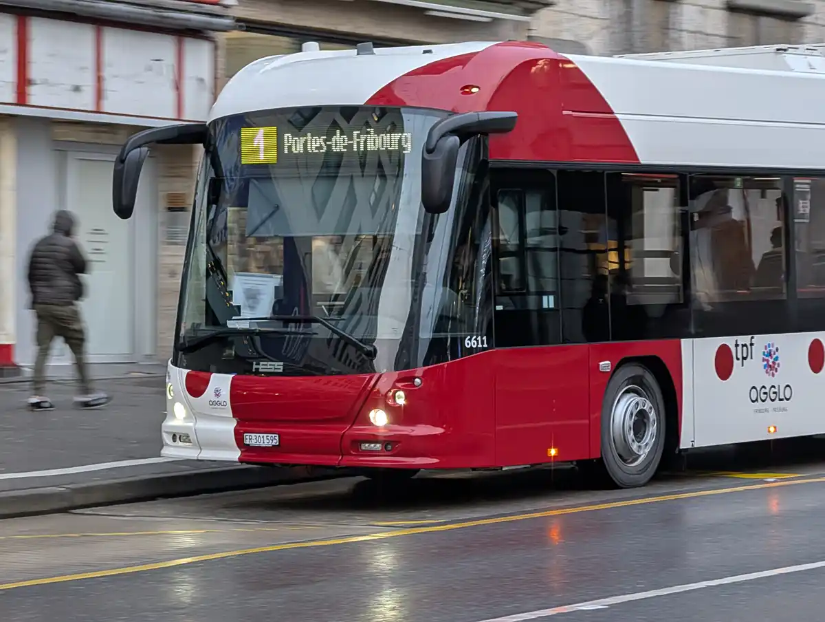 A red and white public bus, marked with route number 1 and destination 'Portes-de-Fribourg', is captured in motion on a wet…