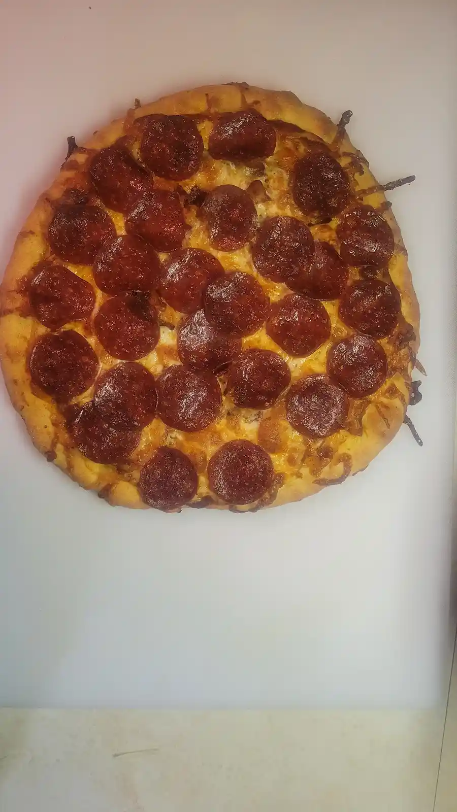 A top-down photo of a round pepperoni pizza with melted cheese and a golden-brown crust, resting on a white surface. The…