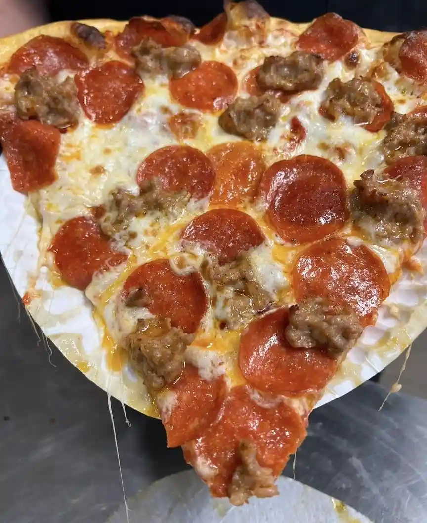 a close-up photo shows a slice of pepperoni and sausage pizza being held up, with melted cheese stretching from the slice to…