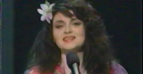 A woman with long dark hair and a white flower in her hair is speaking into a microphone. The overlaid text reads: 'i'm not…