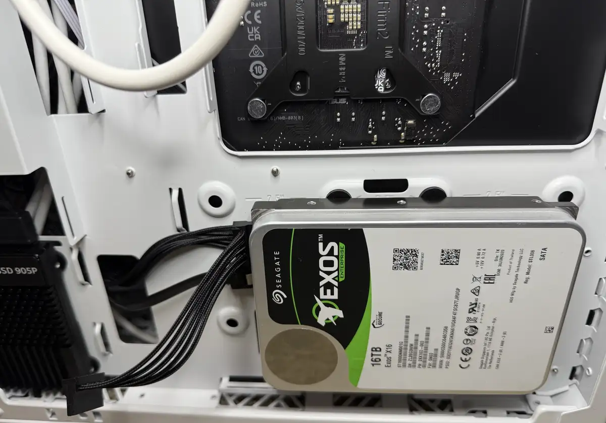 A close-up photo of the inside of a white computer case showing a Seagate Exos X16 16TB enterprise hard drive installed in a…