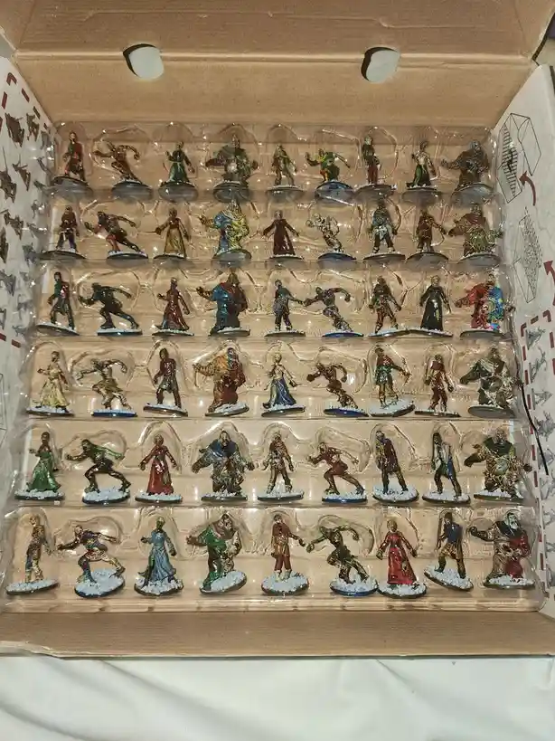 An open cardboard box contains a clear plastic tray holding dozens of painted miniature figurines, all depicting various…