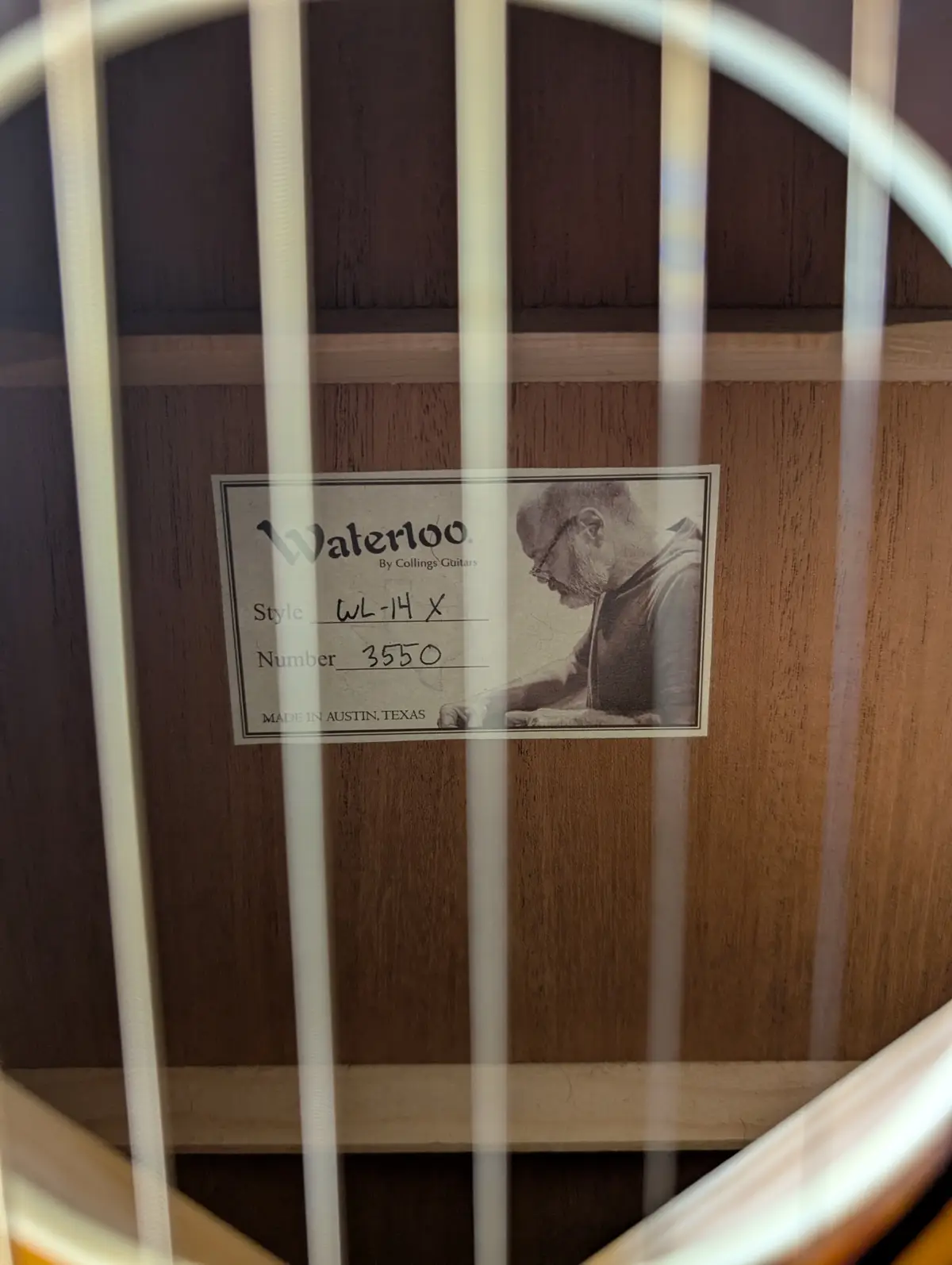 A close-up photo of a guitar's interior label, partially obscured by the strings, showing 'Waterloo. By Collings Guitars…