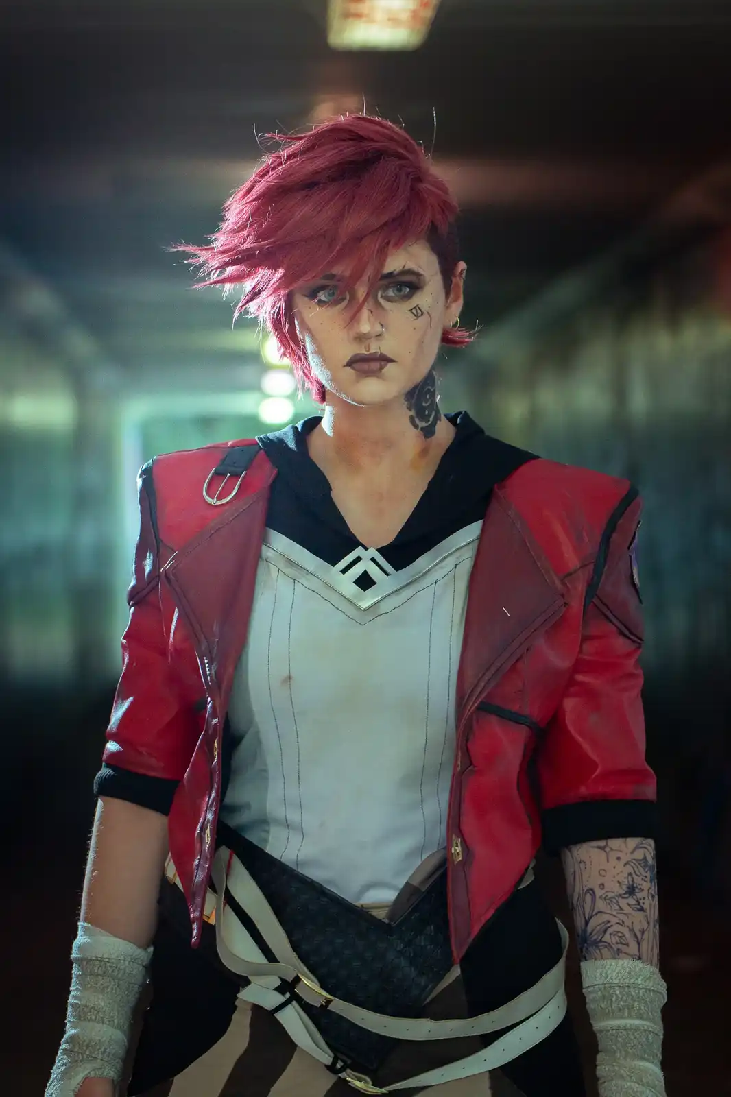 A person in cosplay as the character Jinx from League of Legends, wearing a red jacket, white top, and black pants with…
