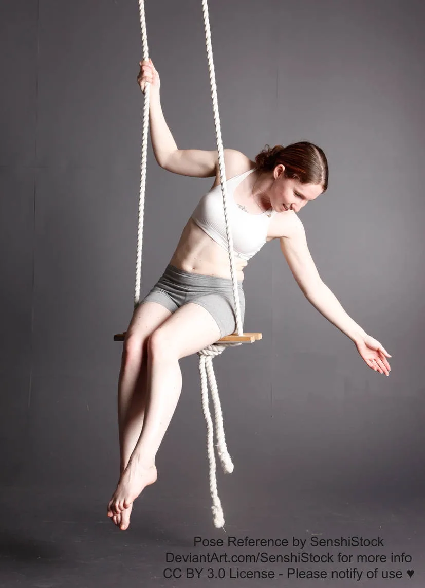 A woman in a white sports bra and grey shorts is suspended in a studio on a rope swing, holding one rope with her right hand…
