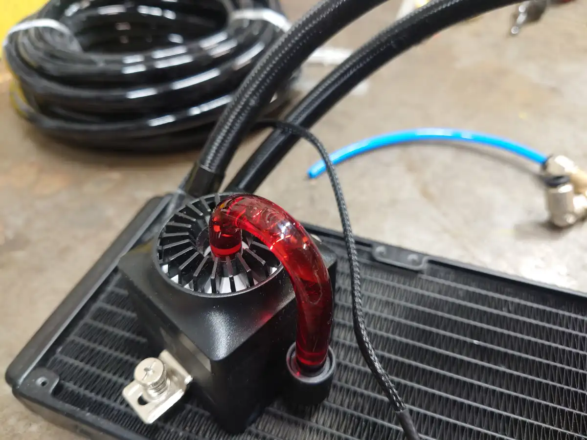 A close-up photo of a custom PC liquid cooling system with a red translucent coolant tube curving over a black radiator fan…