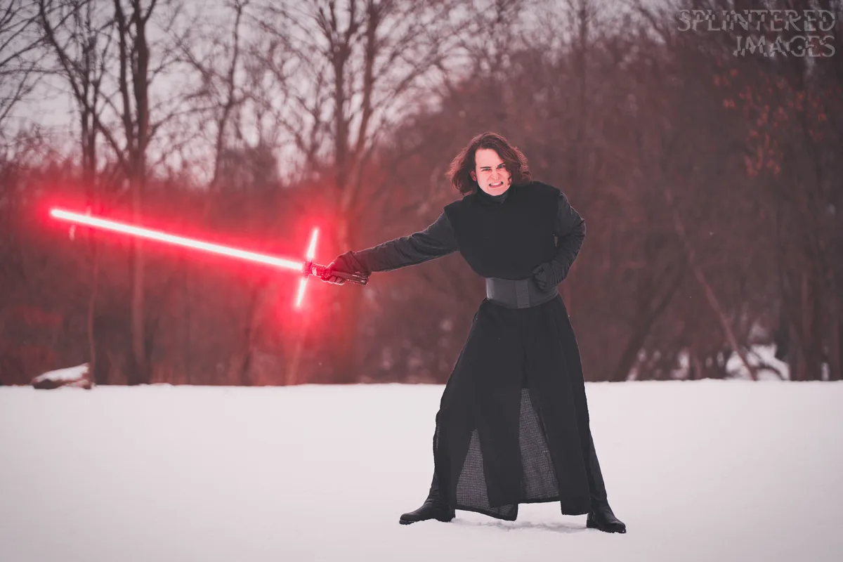 A person dressed as Kylo Ren from Star Wars stands in a snowy field, holding a red lightsaber and making an angry, snarling…
