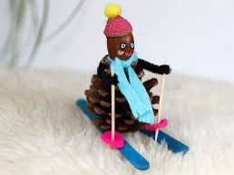 A pinecone is dressed as a skier with a pink hat, blue scarf, and is strapped to blue skis with pink bindings, sitting on a…
