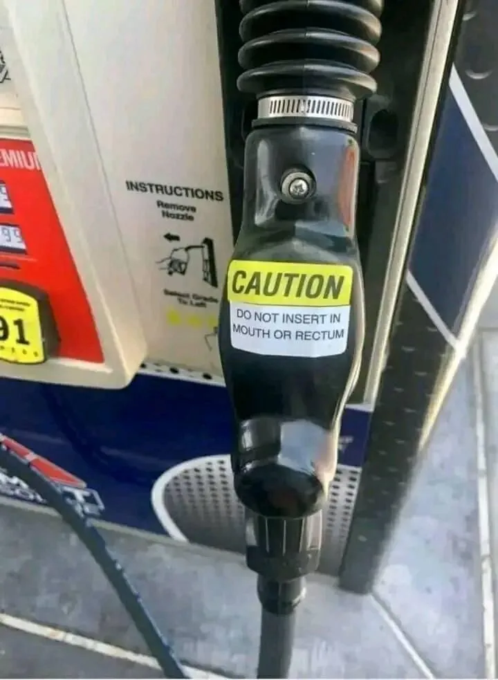 A close-up photo of a black gas pump nozzle with a yellow and white warning sticker that reads 'CAUTION DO NOT INSERT IN…