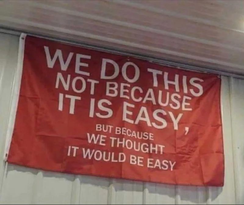 A red banner with white text hangs on a light-colored wall or door, displaying the message 'WE DO THIS NOT BECAUSE IT IS…