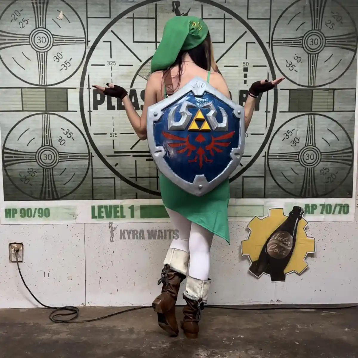A person in a Zelda Link cosplay, wearing a green hat and tunic, stands with their back to the camera holding a Hylian…