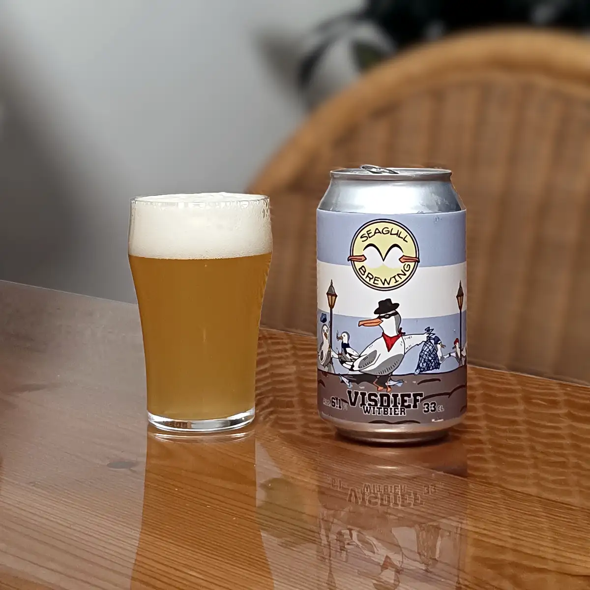 A glass of golden beer with a white head sits next to a silver can of 'Seagull Brewing' beer labeled 'VISDIEF WITBIER 6.1%…