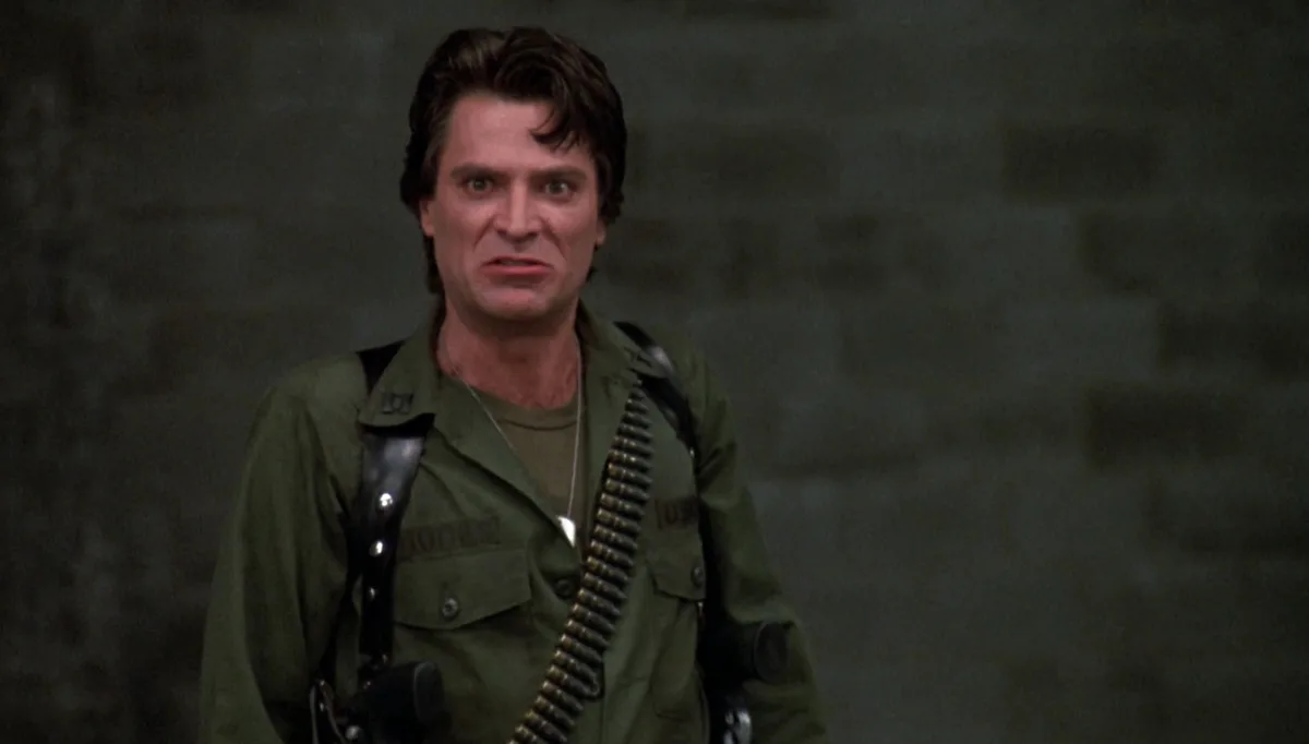 a man in a green military uniform with a bandolier of bullets across his chest stares with a shocked, wide-eyed expression…