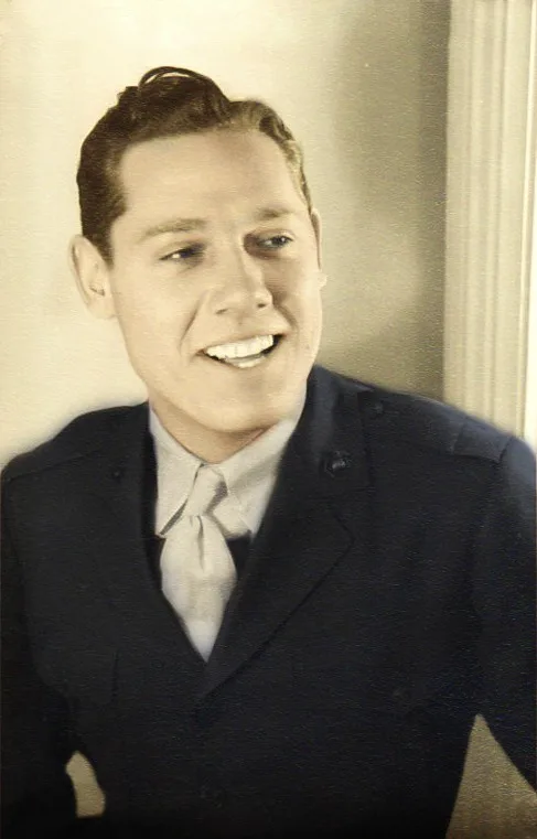 A sepia-toned vintage photo shows a smiling man in a dark suit and light tie, looking slightly to his right. The overlaid…